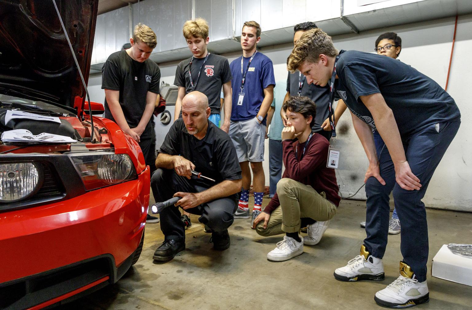 Teen Auto Workshop participants gather around to watch an in-progress repair.
