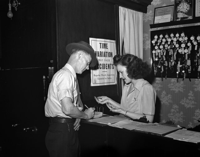 Photograph showing a railroad employee checking the time with a time inspector.
