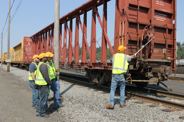 A new employee participates in a hands-on demonstration of the brake stick, showing other new hires how to safely set hand brakes without climbing equipment. 