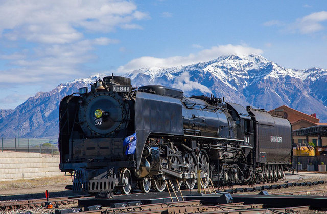 Union Pacific steam locomotive No. 844 traveling along railroad tracks through a rural landscape with trees and hills.
