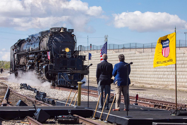 Union Pacific Big Boy No. 4014 steam locomotive approaching on railroad tracks, emitting steam and smoke against a clear sky.