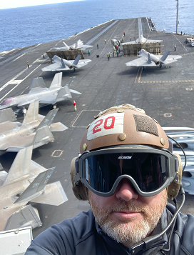 Mark Karpf stands on deck the USS Carl Vinson, wearing a helmet | MR