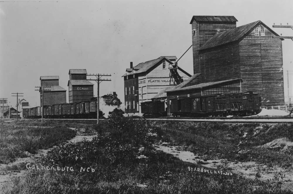 En route steam locomotive passing by a mill in Gothenburg, Nebraska, c 1920