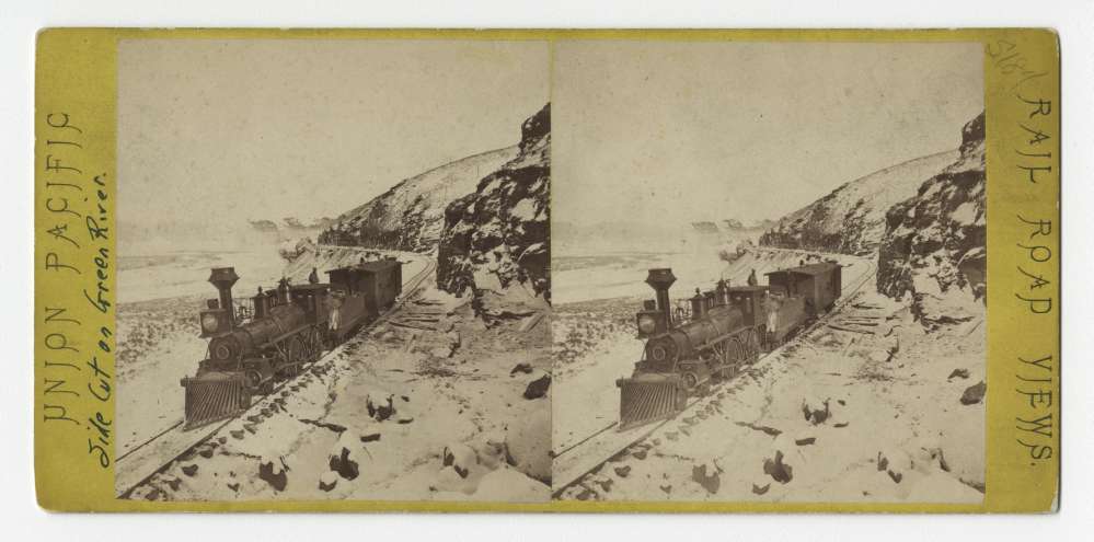 A stereo card showing a steam locomotive passing by the side cut on Green River, Wyoming