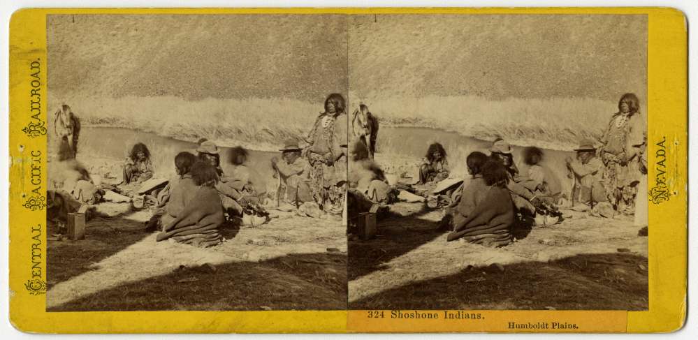 A stereo card showing a group of American Indians from the Shoshone Nation gathered near a river