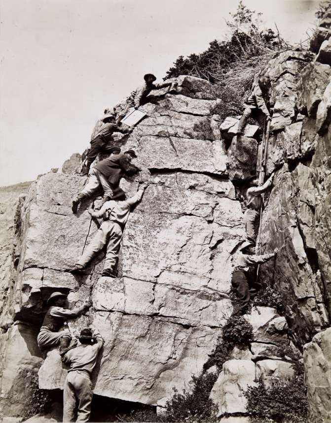 Men scaling a rockface carrying photographic equipment